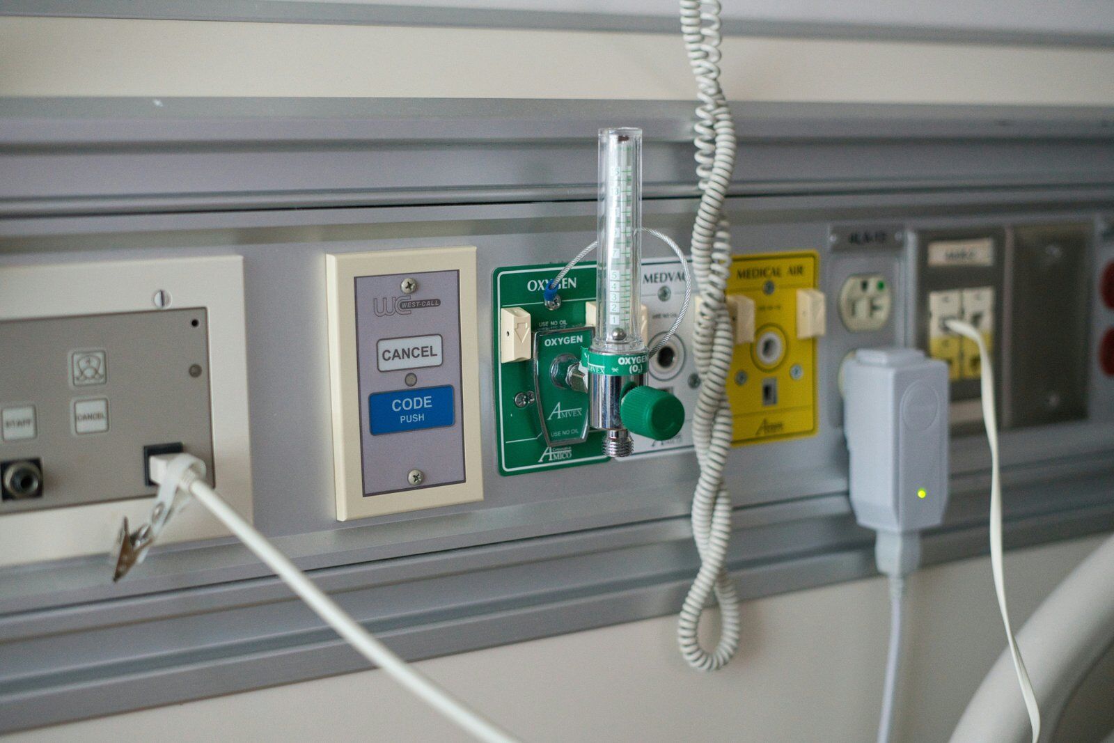 medical-gas-inspections-power-apps-1600 | eSoftware Associates Inc (ESW) Medical gas panel on a hospital wall featuring an oxygen flowmeter and labeled valves, with cords nearby