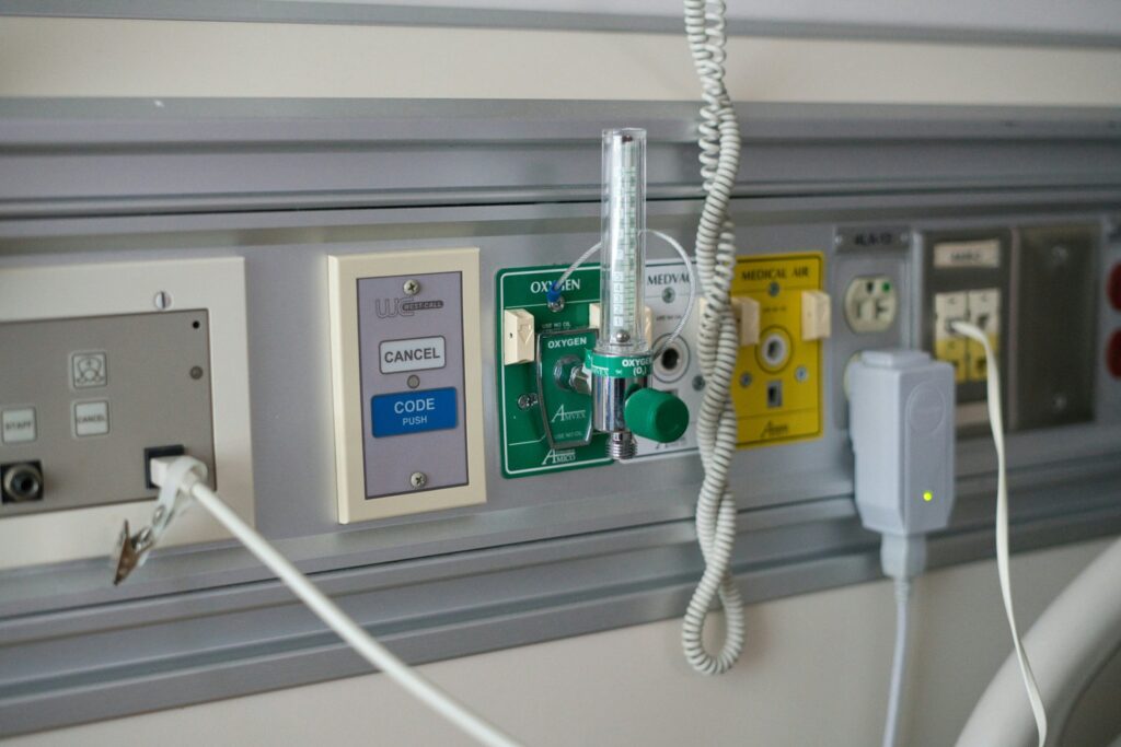 Medical gas panel on a hospital wall featuring an oxygen flowmeter and labeled valves, with cords nearby
